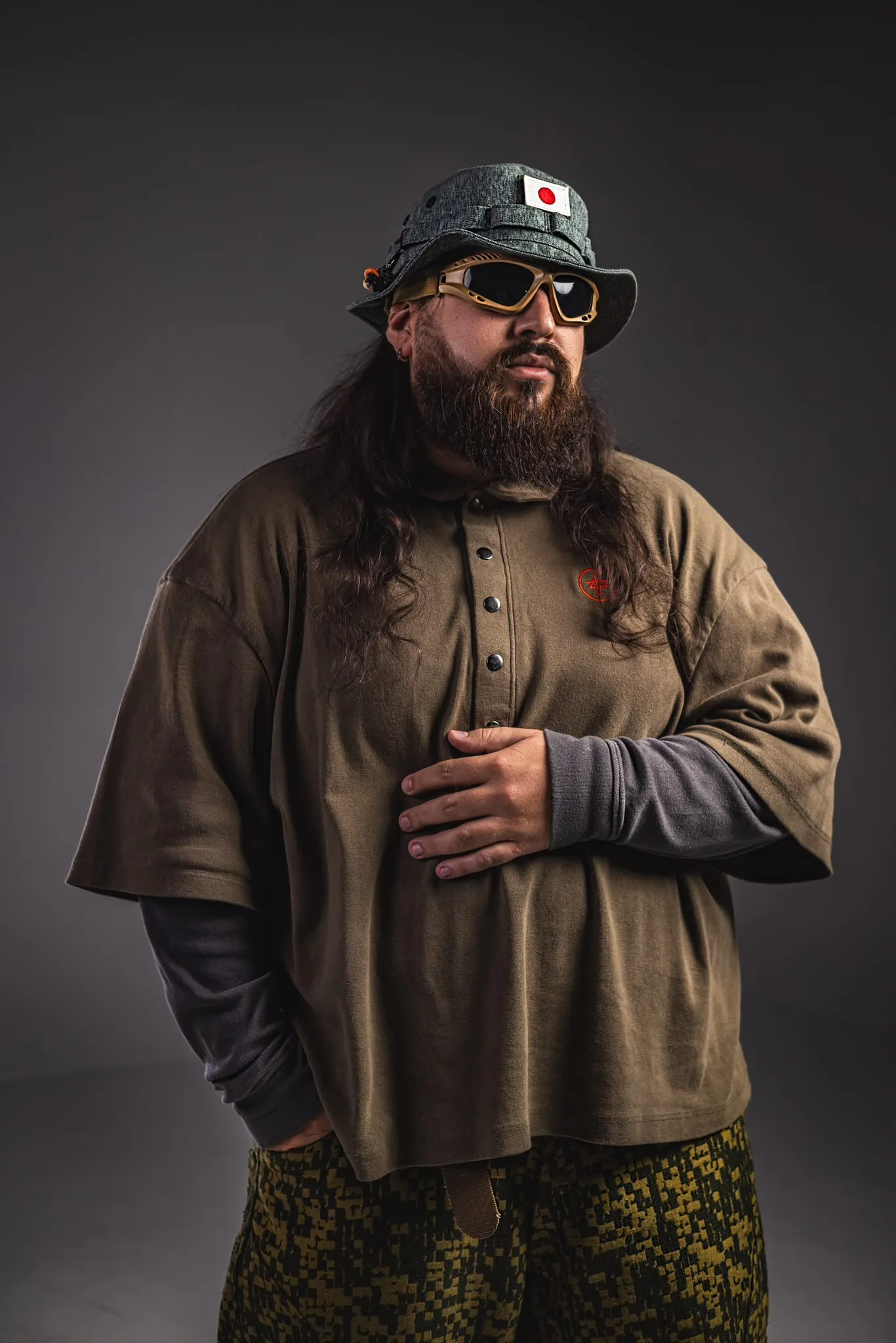 Armando “Mandi” Pereira in the studio, wearing a bucket hat with a Japanese flag patch and an olive polo with the APEREIRA symbol